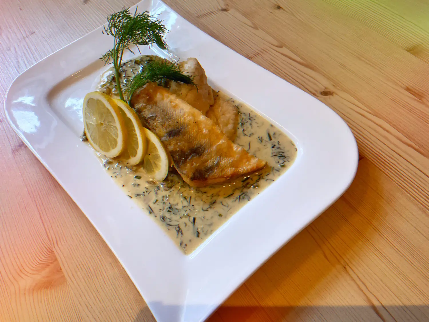 Gebratener Fisch, vermutlich eine Weißfischart, serviert mit einer cremigen Dillsauce, garniert mit frischem Dill und Zitronenscheiben Restaurant Topinambur