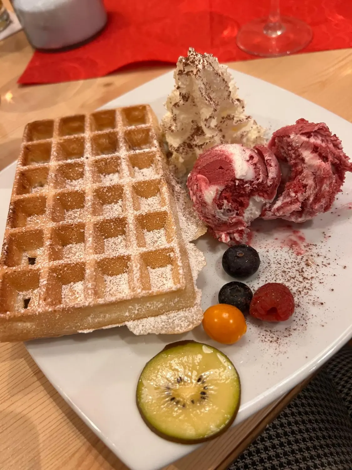 Restaurant Topinambur: Ein Dessert mit einer Waffel, serviert mit Eis, Schlagsahne und frischen Früchten, darunter Blaubeeren, Himbeeren, Kumquats und einer Kiwischeibe