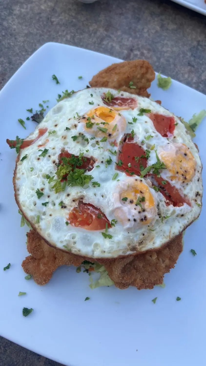 Eine Schnitzelvariation mit Spiegeleiern und Tomatenwürfeln, garniert mit Kräutern. Restaurant Topinambur